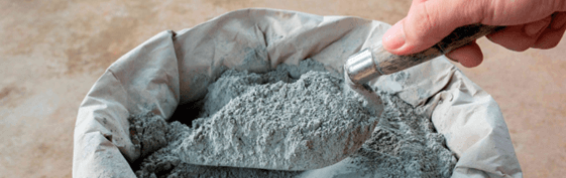 Foto de mão mexendo em saco de cimento com uma pá de pedreiro