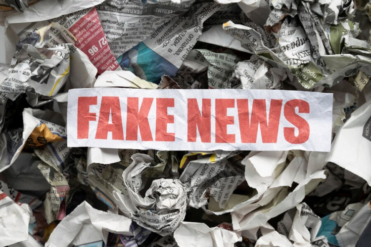 #ParaTodosVerem A imagem mostra um fundo com folhas de jornal amassadas e um pedaço de papel branco em que se lê, em vermelho, “fake news”