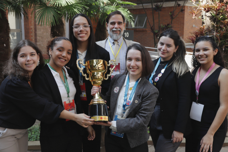 #ParaTodosVerem Seis mulheres jovens e um homem de meia idade na foto, todos estão sorrindo. Duas estão segurando o troféu.