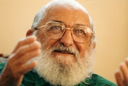 Paulo Freire sorrindo com as mãos levemente suspensas