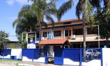 imagem de um prédio de dois andares de portão azul, árvores em seu terreno e algumas bandeiras