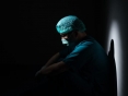 Um profissional da saúde vestido com EPIs sentado no chão, em um lugar escuro