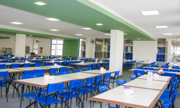 Foto do interior do restaurante universitário da UFF, com mesas brancas e cadeiras azuis dispostas pelo salão para a acomodação da comunidade universitária