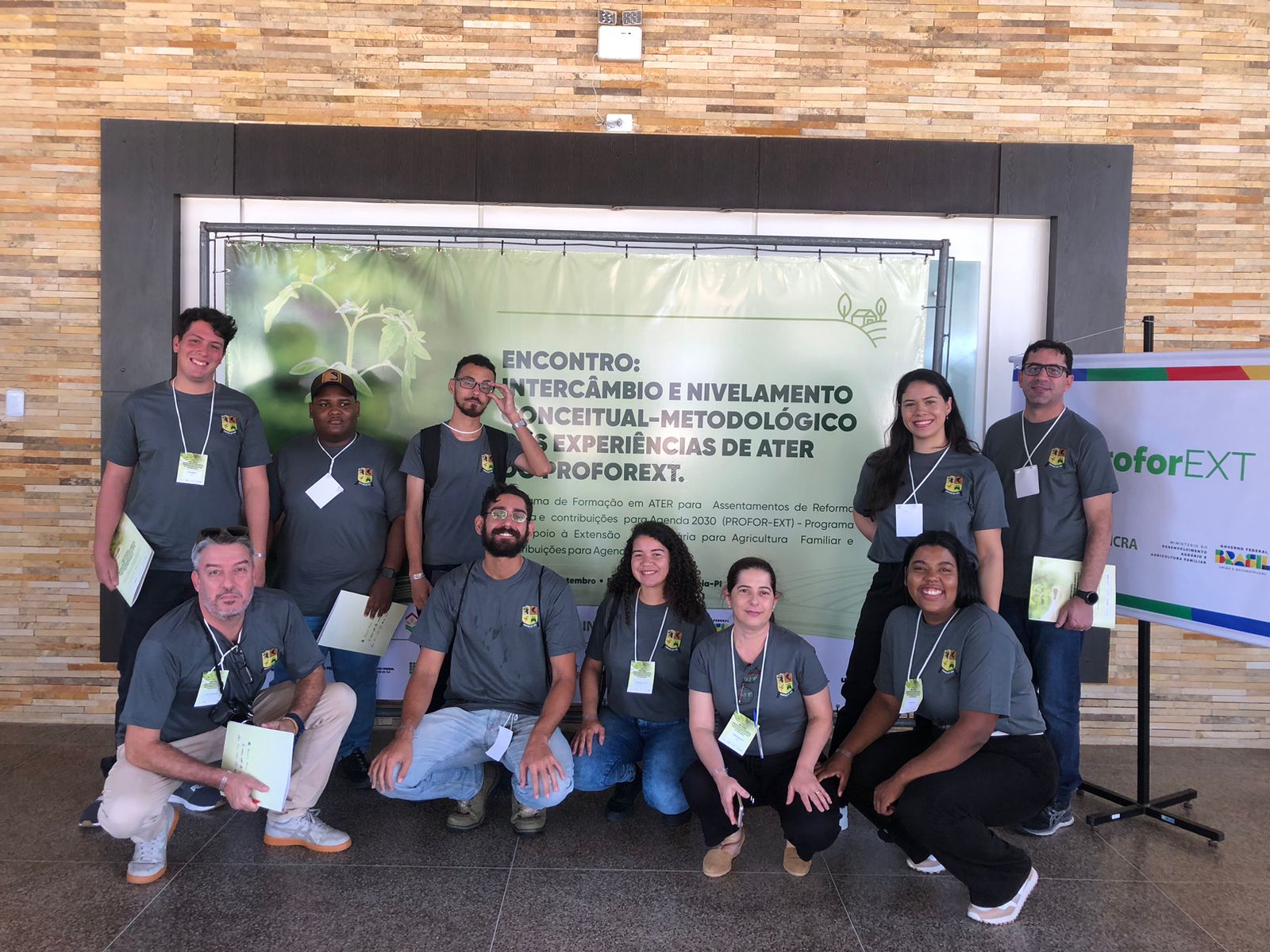 Foto da equipe da UFF, composta por 6 homens e 4 mulheres uniformizados com uma camisa cinza, em frente ao painel do evento