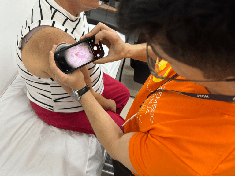 Imagem de um médico utlizando um aparelho para visualizar a pele de uma paciente idosa